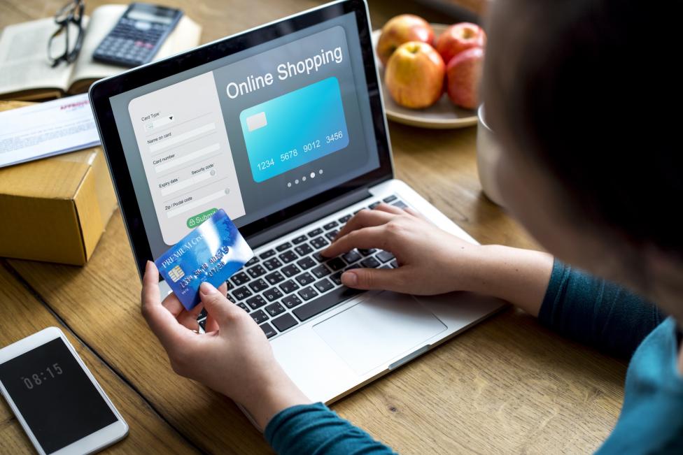 E-Commerce: Frau bezahlt mit einer Kreditkarte an einem Laptop
