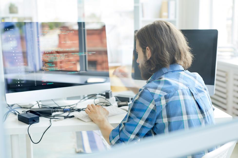 Webhosting: Mann arbeitet an einem Computer hinter einer Glaswand
