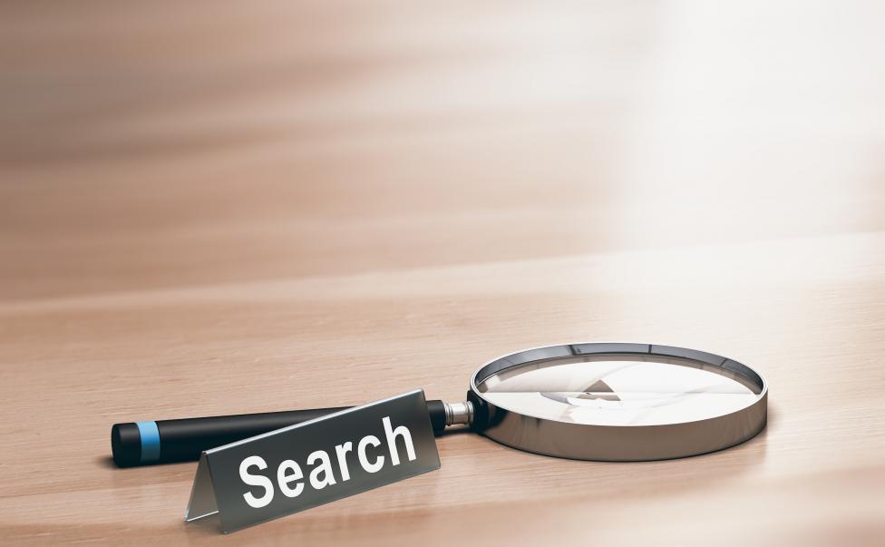 Suchmaschinenoptimierung: Lupe auf Schreibtisch mit Search-Schild